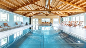 Una piscina interior con vigas de madera, paredes de vidrio transparente y asientos a lo largo de los bordes.
