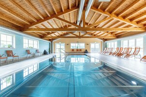 Una piscina interior con vigas de madera, paredes de vidrio transparente y asientos a lo largo de los bordes.