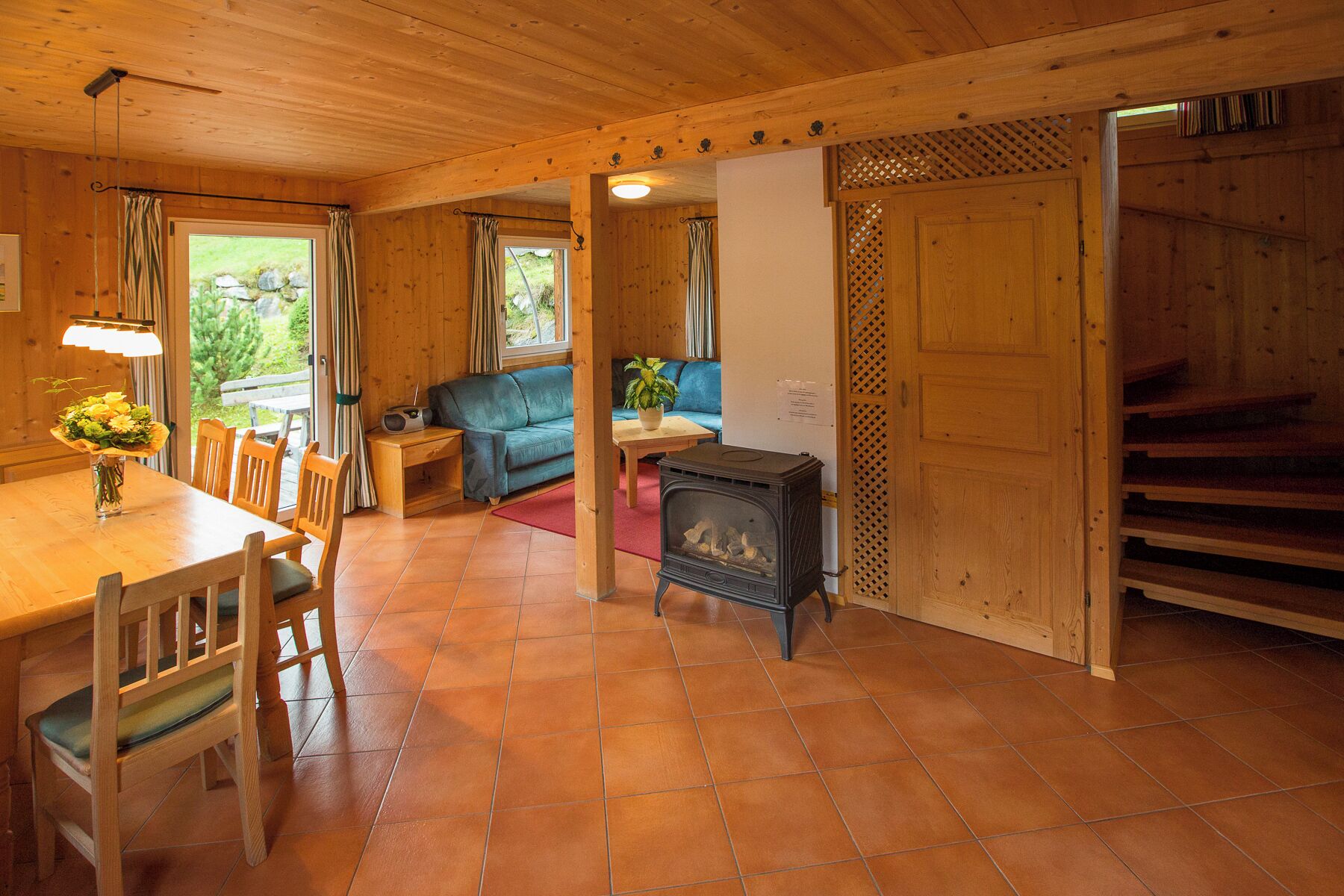 Un intérieur en bois comprenant une table à manger, des chaises, un canapé, une petite table avec une plante et un poêle à bois.