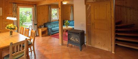 Un intérieur en bois comprenant une table à manger, des chaises, un canapé, une petite table avec une plante et un poêle à bois.