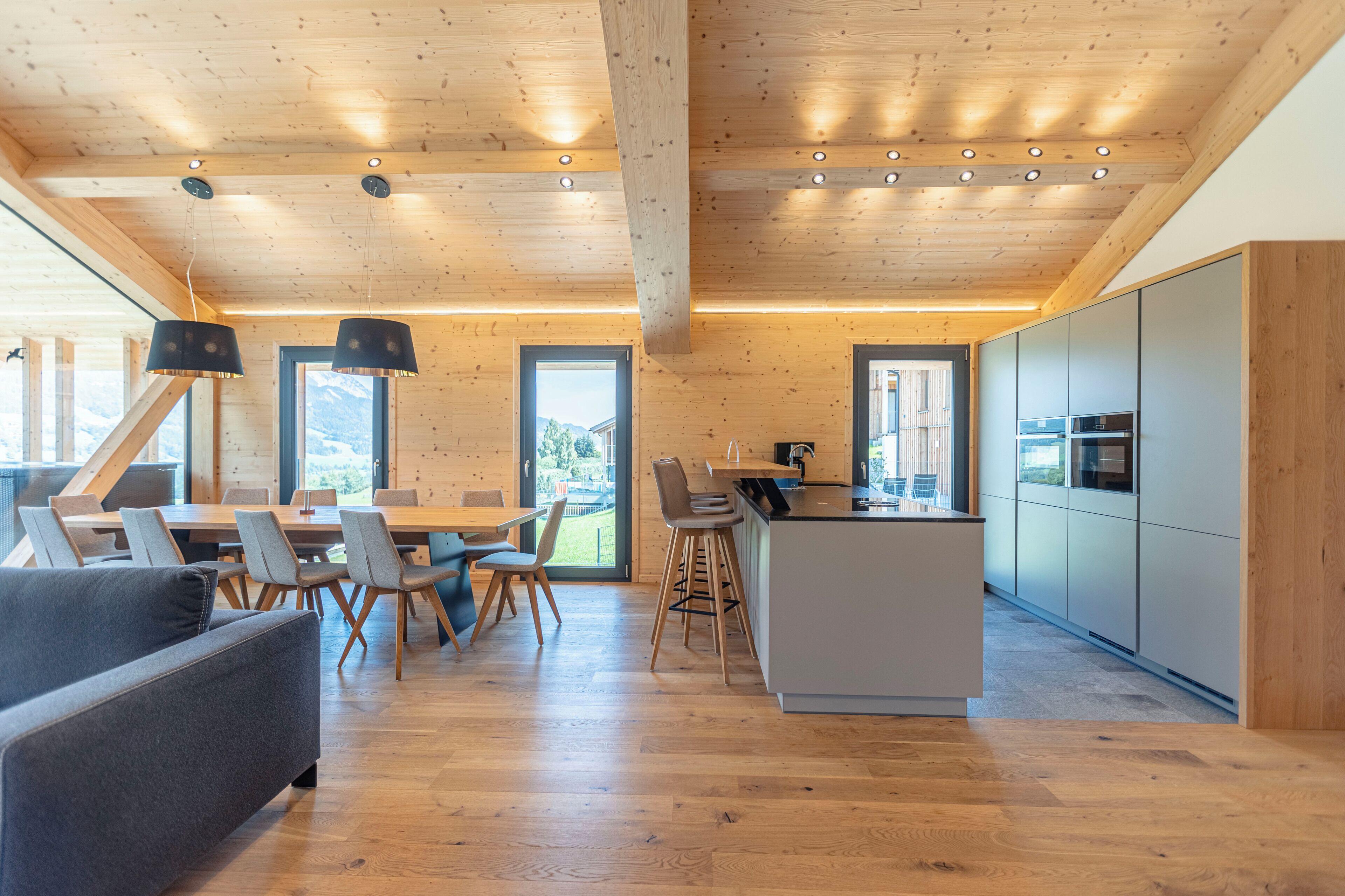 Una cocina moderna con armarios de madera y una isla central, un comedor con una mesa grande y sillas, y una zona de estar acogedora con un sofá.