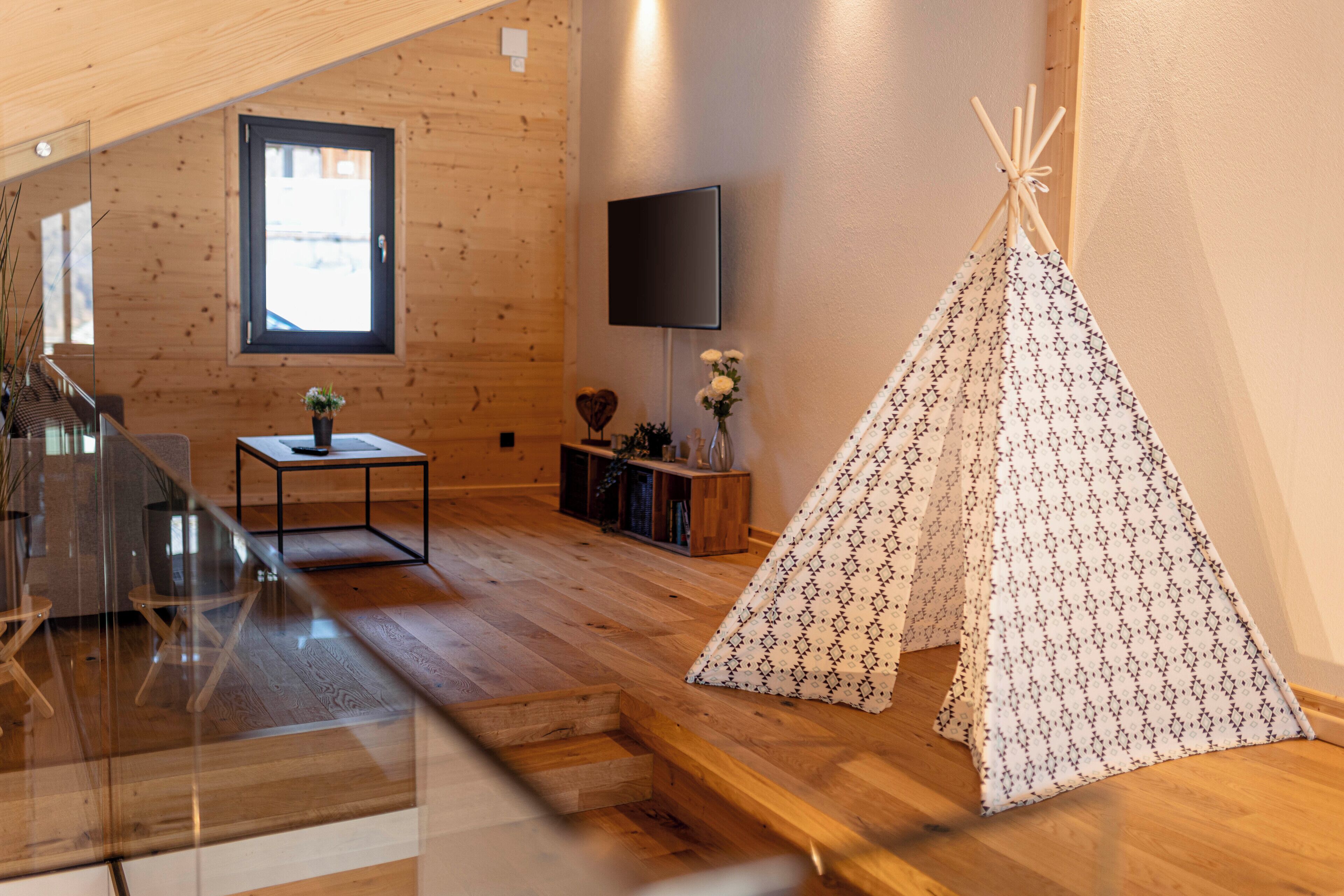 En inredning med trädetaljer, ett tv-appar, ett litet bord med en vas och ett tipi-tält.