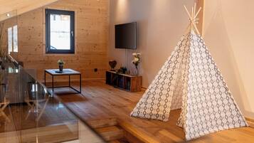 A wooden interior with a TV, a small table with a vase, and a teepee.