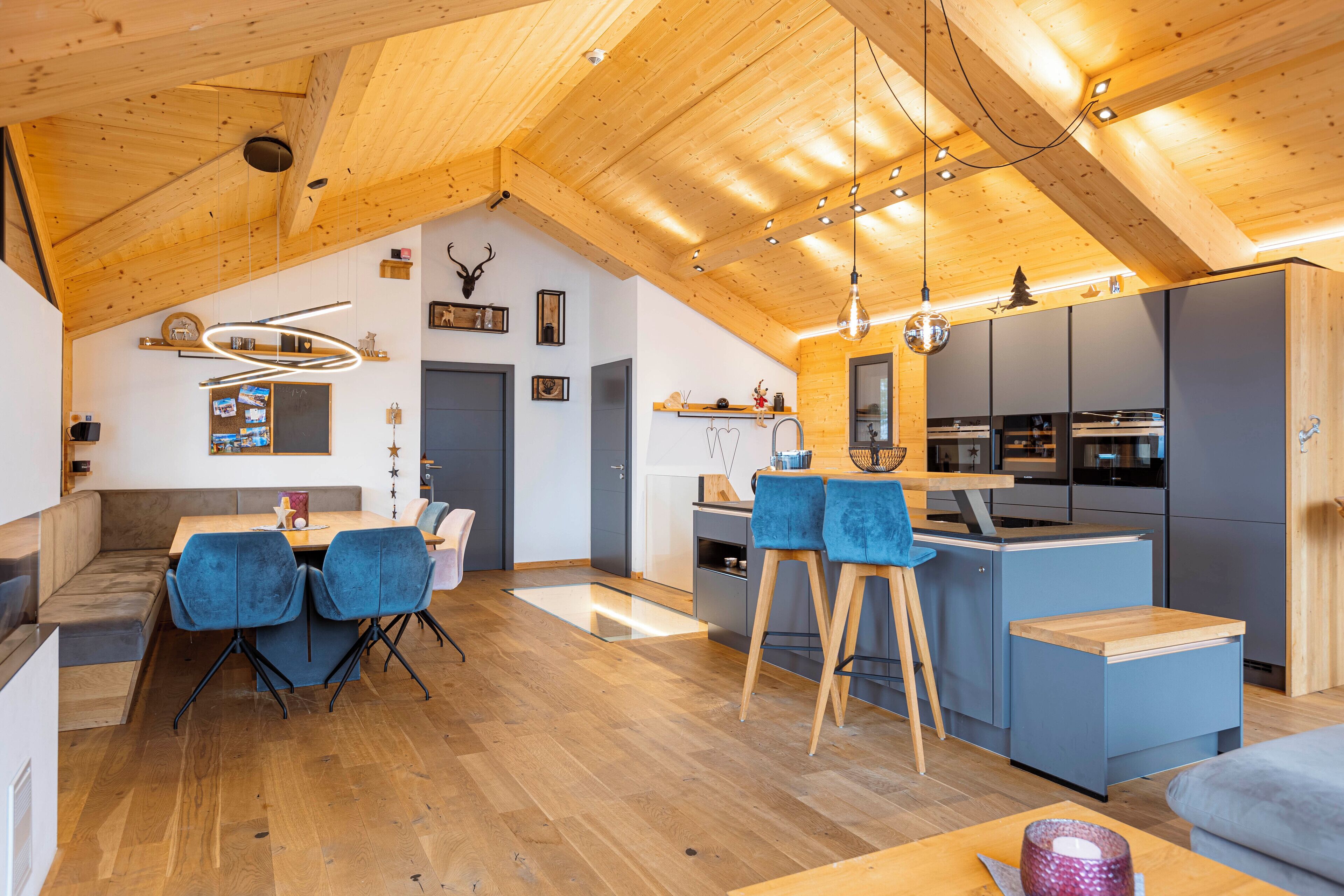 A modern kitchen with a central island, wooden ceiling beams, and a dining area with blue chairs.