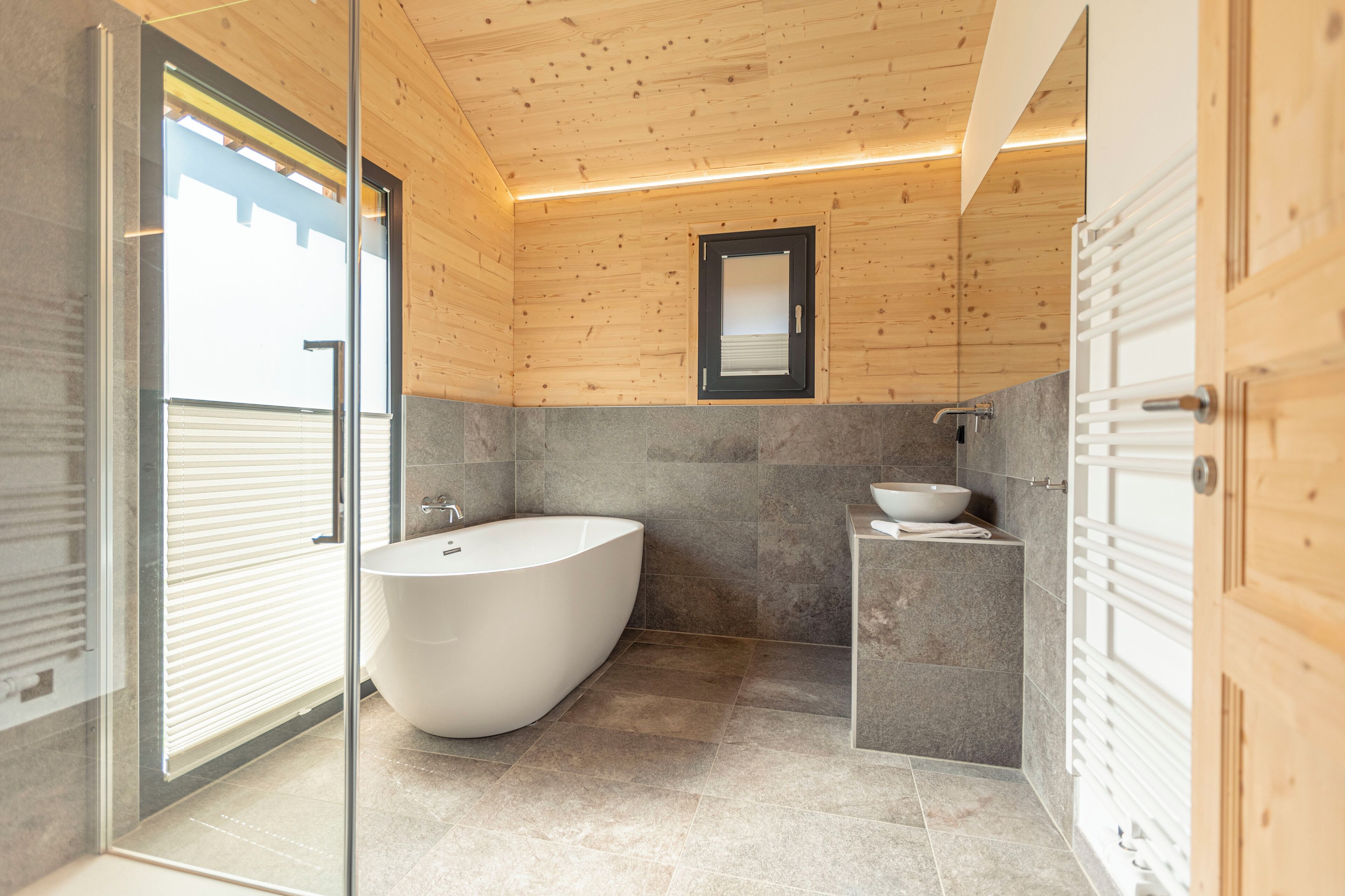 Ein modernes Badezimmer mit freistehender Badewanne, einem kleinen Waschbecken und einem Spiegel an der Wand.