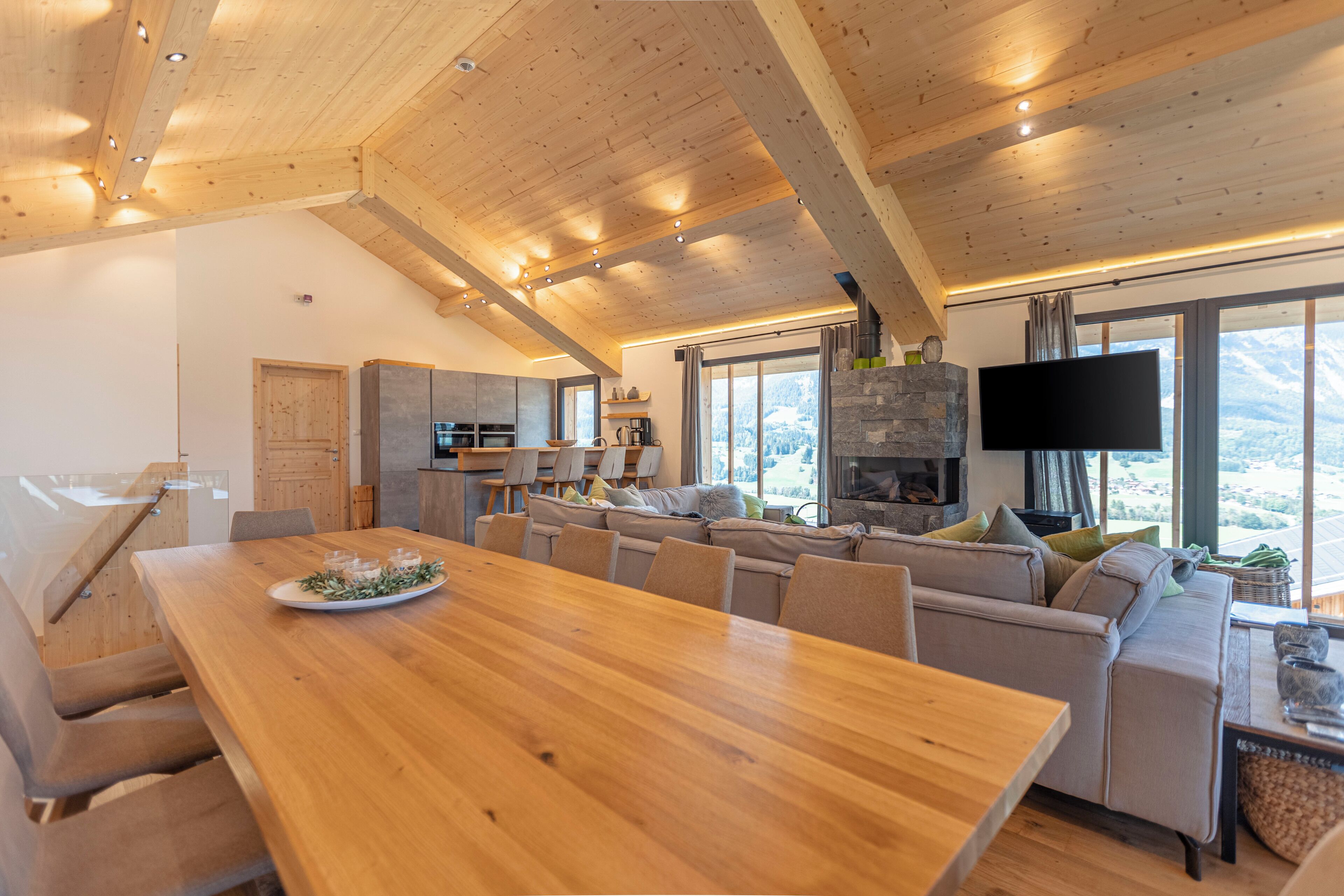 A modern interior with a wooden dining table, a sofa, and a kitchen area.