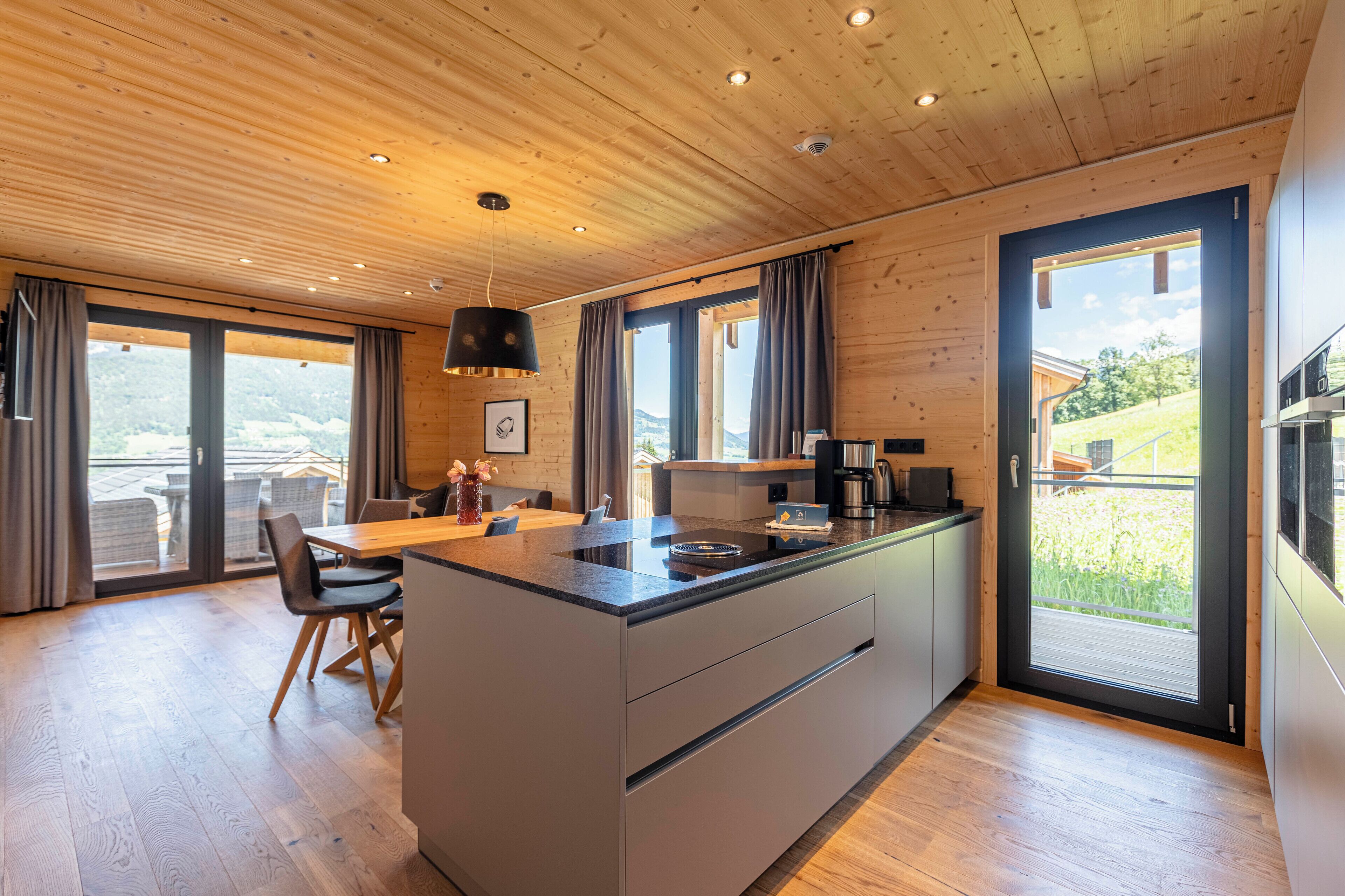 Una cocina moderna con una isla central, techo de madera, ventanas grandes y vistas al exterior.
