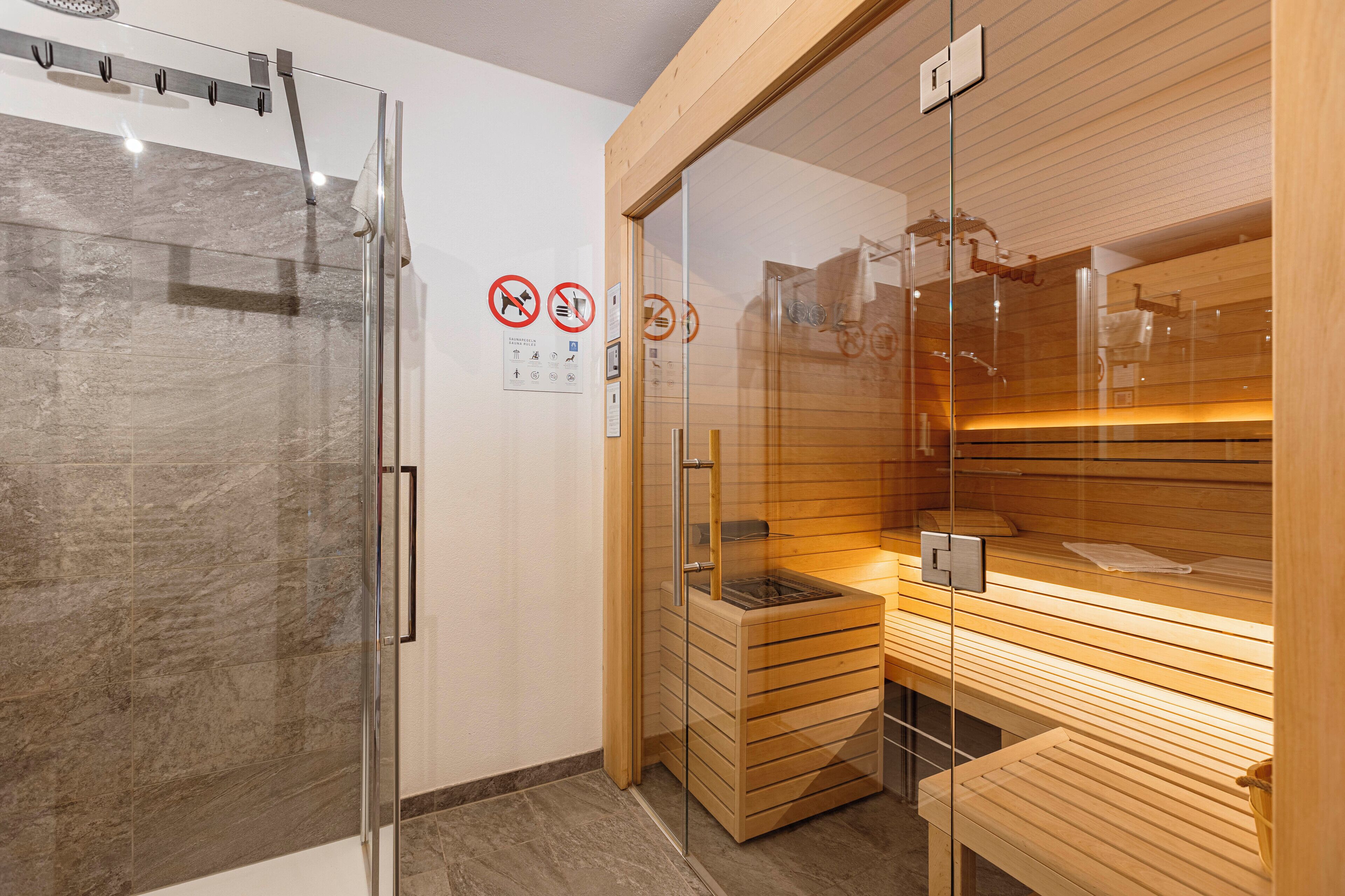 A modern bathroom with a glass shower enclosure, a sauna area with wooden benches, and a tiled floor.