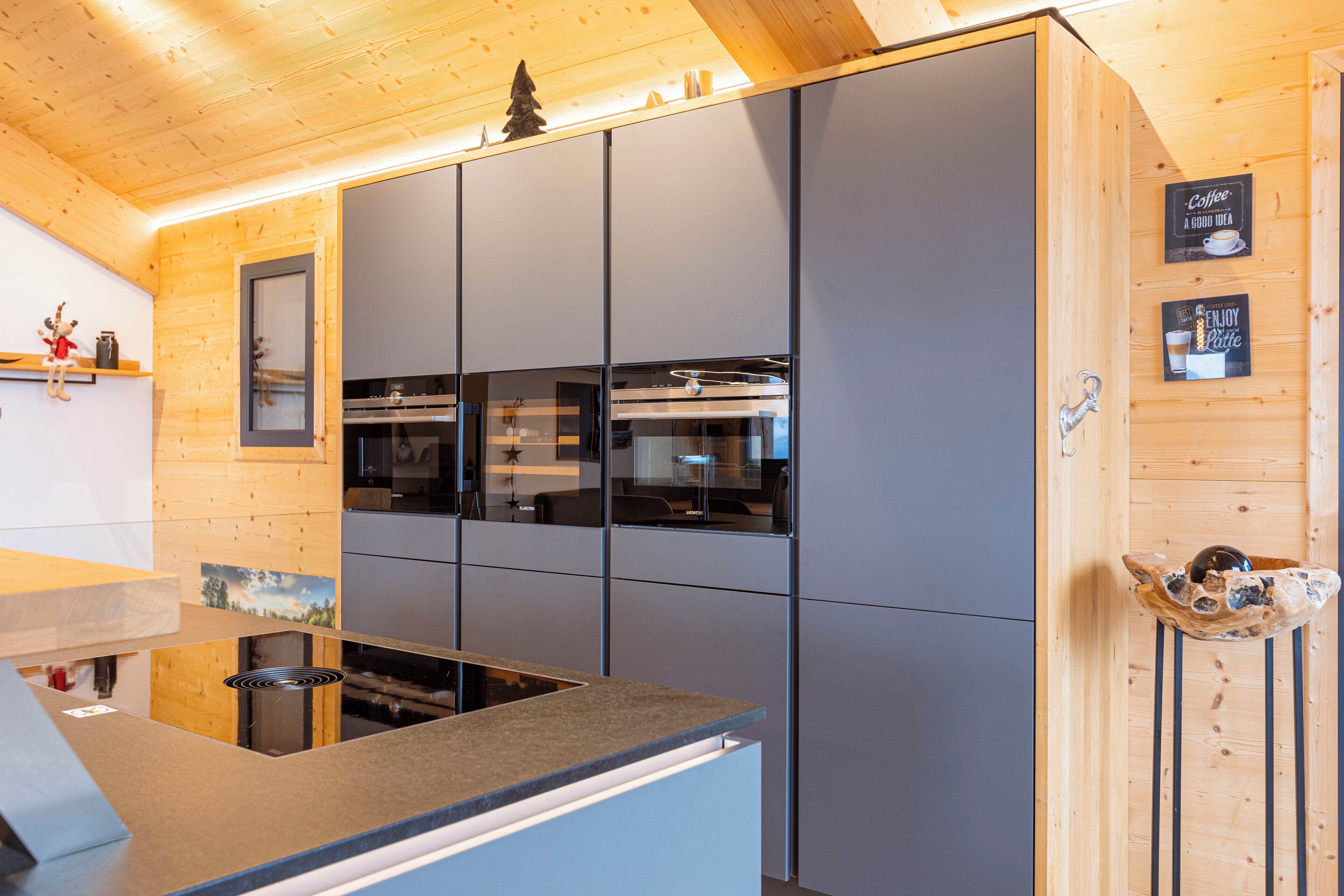 A modern kitchen with a built-in stove, a large refrigerator, and a wooden ceiling.