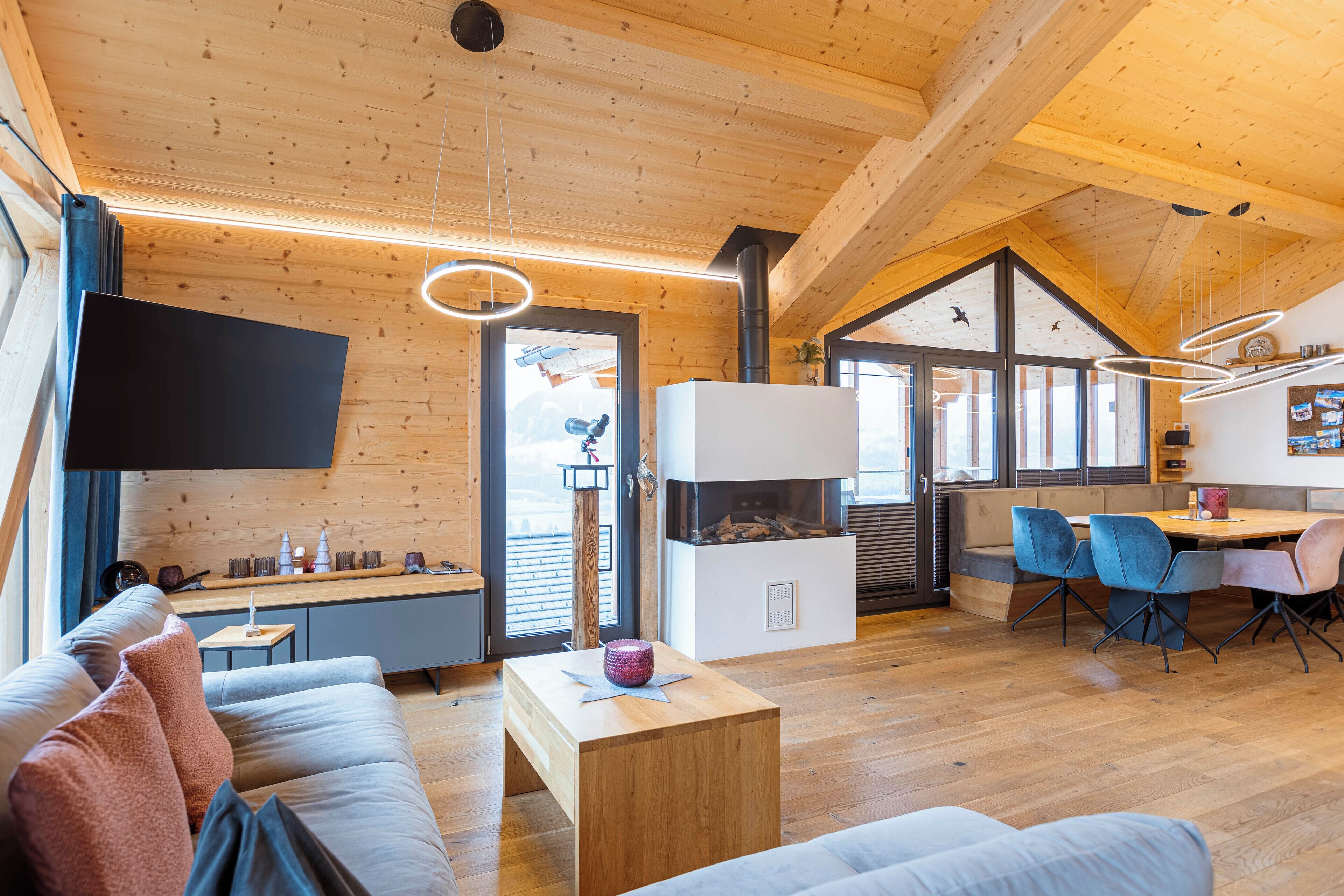 Un interior moderno con techo de madera, un televisor de pantalla plana, una zona de comedor con sillas y una chimenea.