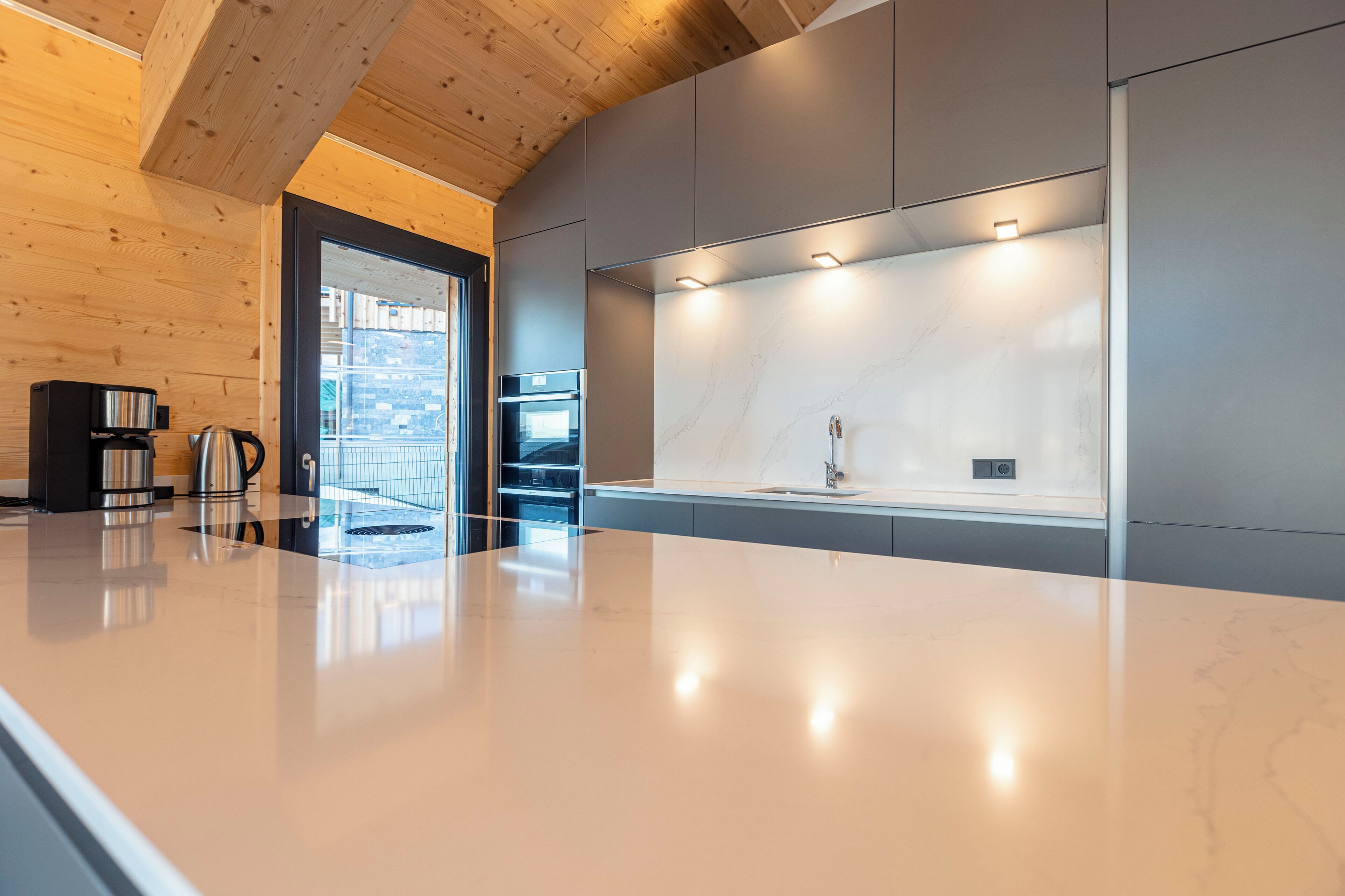 A modern kitchen with a marble countertop, built-in oven, and under-cabinet lighting.
