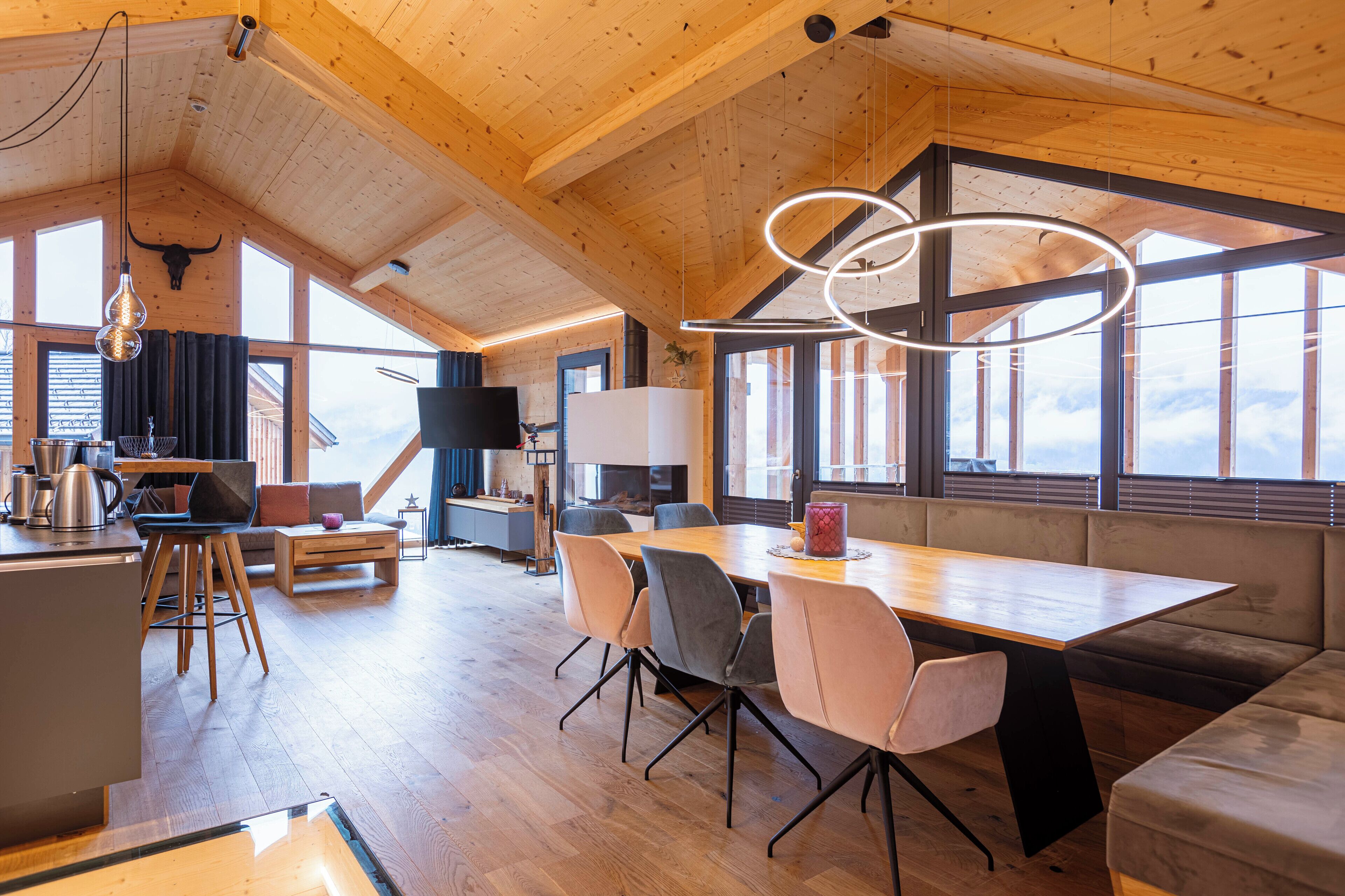A spacious room with a wooden ceiling, large windows, a dining table, and a sofa.