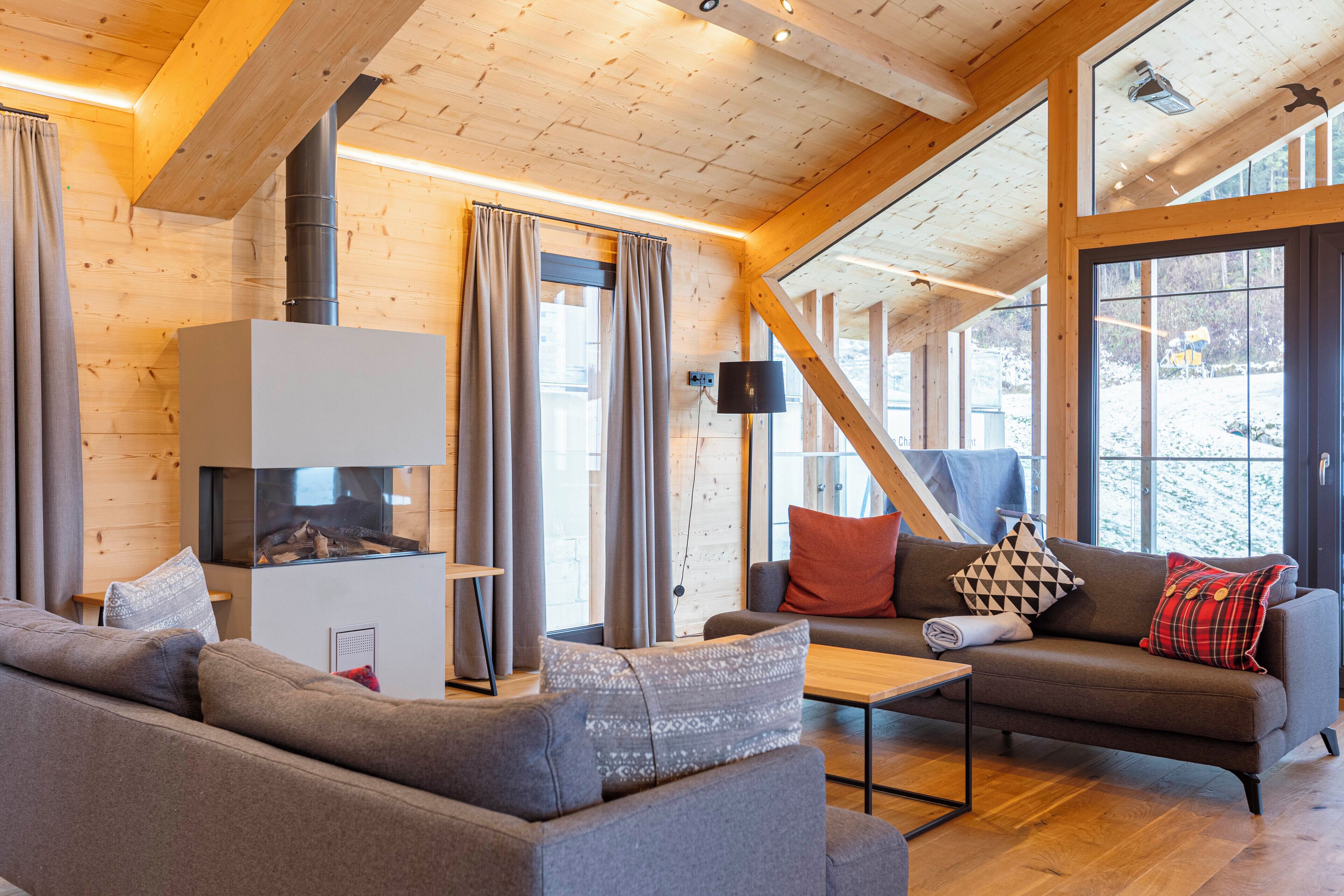 A cozy living room with a fireplace, wooden walls, and large windows.