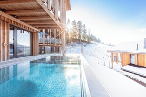 A wooden building with a glass-enclosed pool and a snowy landscape in the background. - Bergresort Hauser Kaibling by ALPS RESORTS (Haus)