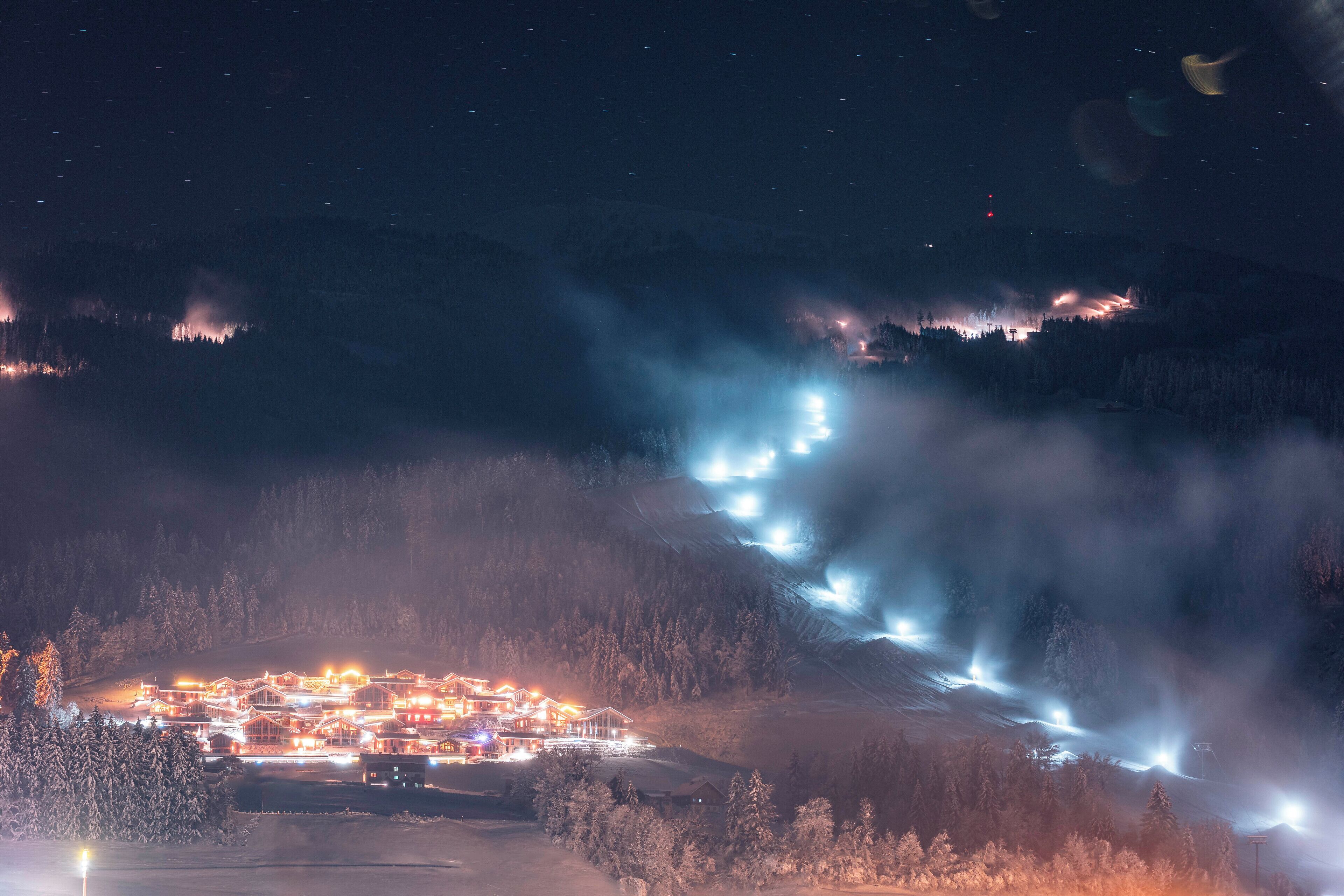 Un pueblo de montaña cubierto de nieve, con edificios iluminados y un telesilla.