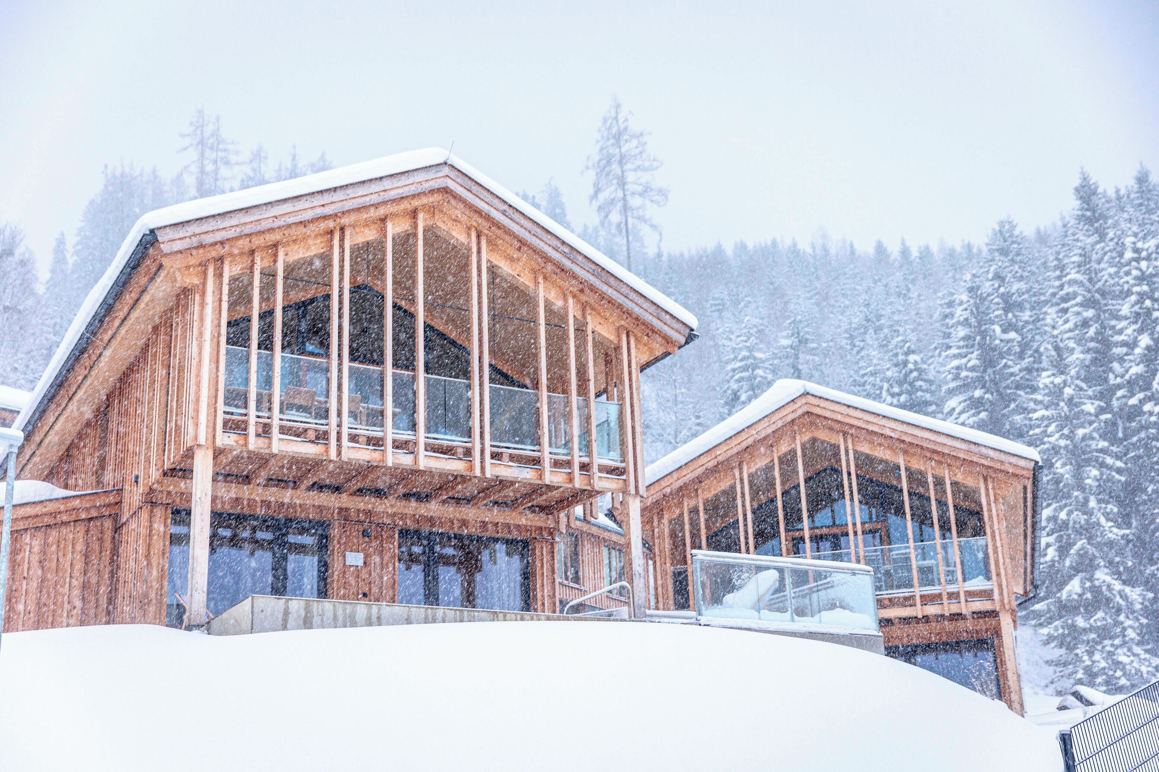 A wooden cabin with large windows and a balcony, surrounded by snow-covered trees.
