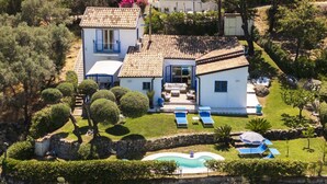 Une maison à deux étages avec une piscine, un espace salon extérieur et un mur en pierre.