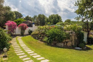 A stone pathway leading to a house with a stone wall and lush greenery.