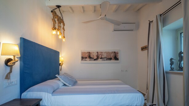 Un dormitorio con cama, ventilador de techo, lámpara de pared y un cuadro enmarcado.
