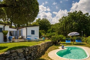 A pool with lounge chairs, a stone wall, and a white building with blue shutters. - Villa Acquaro Santa Caterina  (Santa Caterina dello Ionio)
