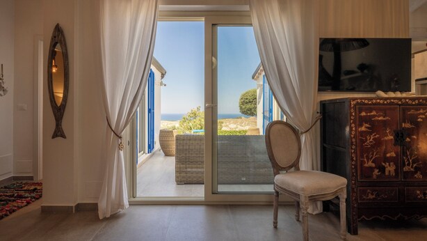Une chambre dotée d’une porte-fenêtre coulissante donnant sur un balcon, d’une chaise, d’un téléviseur et d’un meuble décoratif.