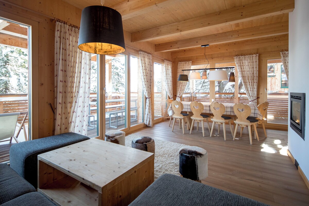 A cozy cabin interior with a wooden dining table, chairs, and a sofa.