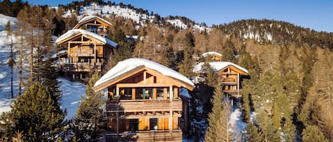 Una cabaña de madera con varios balcones, rodeada de árboles nevados y un telón de fondo montañoso.