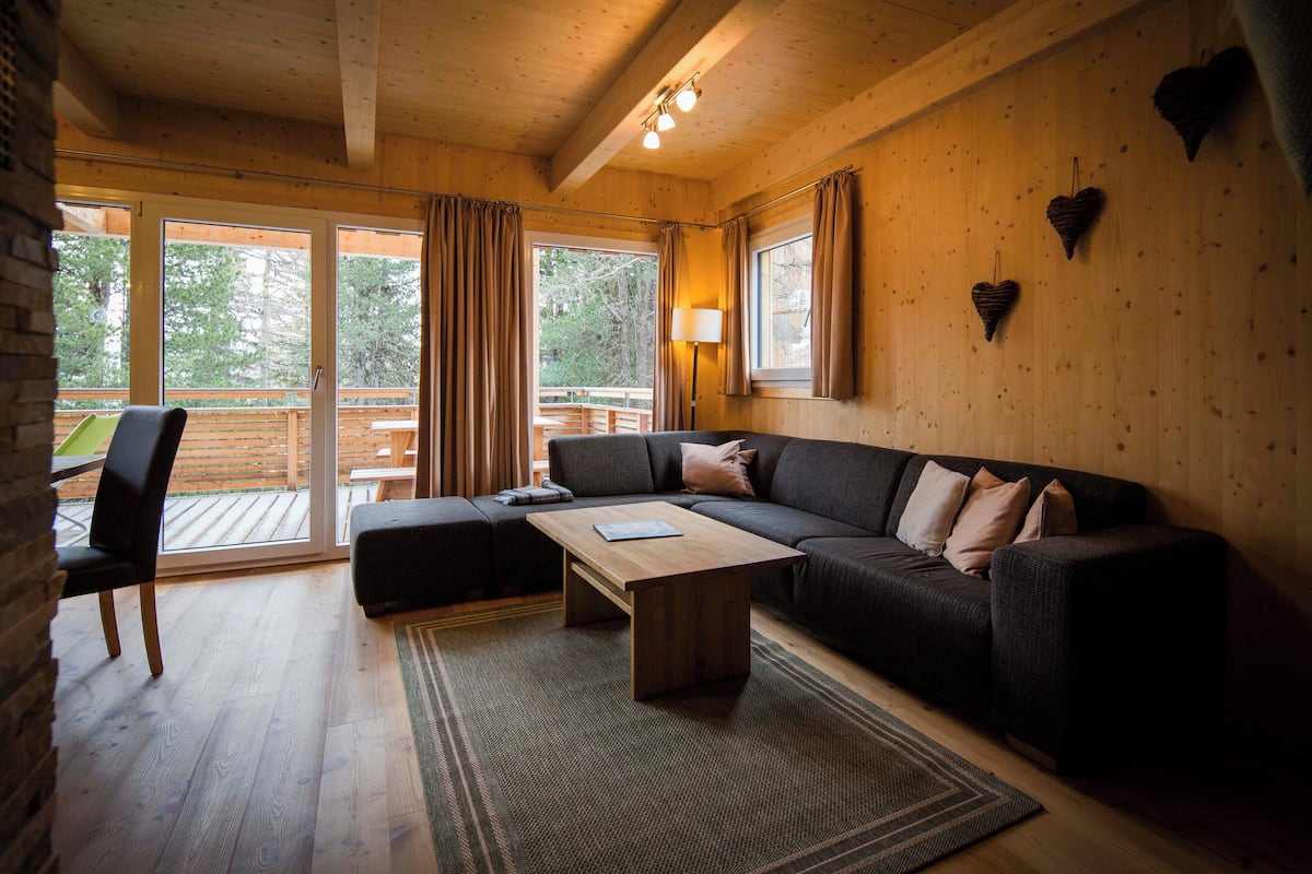 A cozy living room with a dark-colored sofa, a wooden coffee table, and a view of the outdoors through large sliding glass doors.