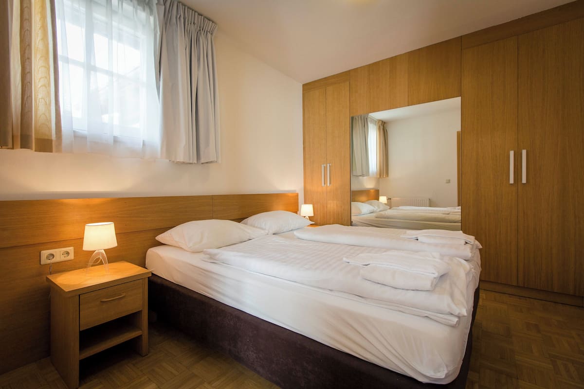 A hotel room with a large bed, a bedside table with a lamp, wooden wardrobe, and a mirror.