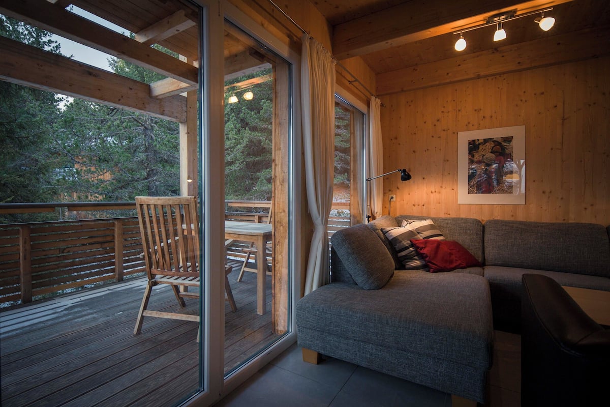 A cozy cabin interior with a wooden deck, a sofa with cushions, and a dining area.