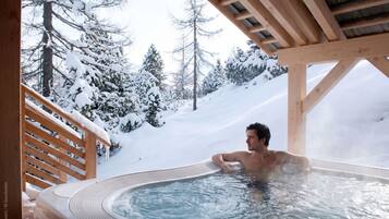 A person relaxing in a hot tub with a snowy mountainous backdrop.