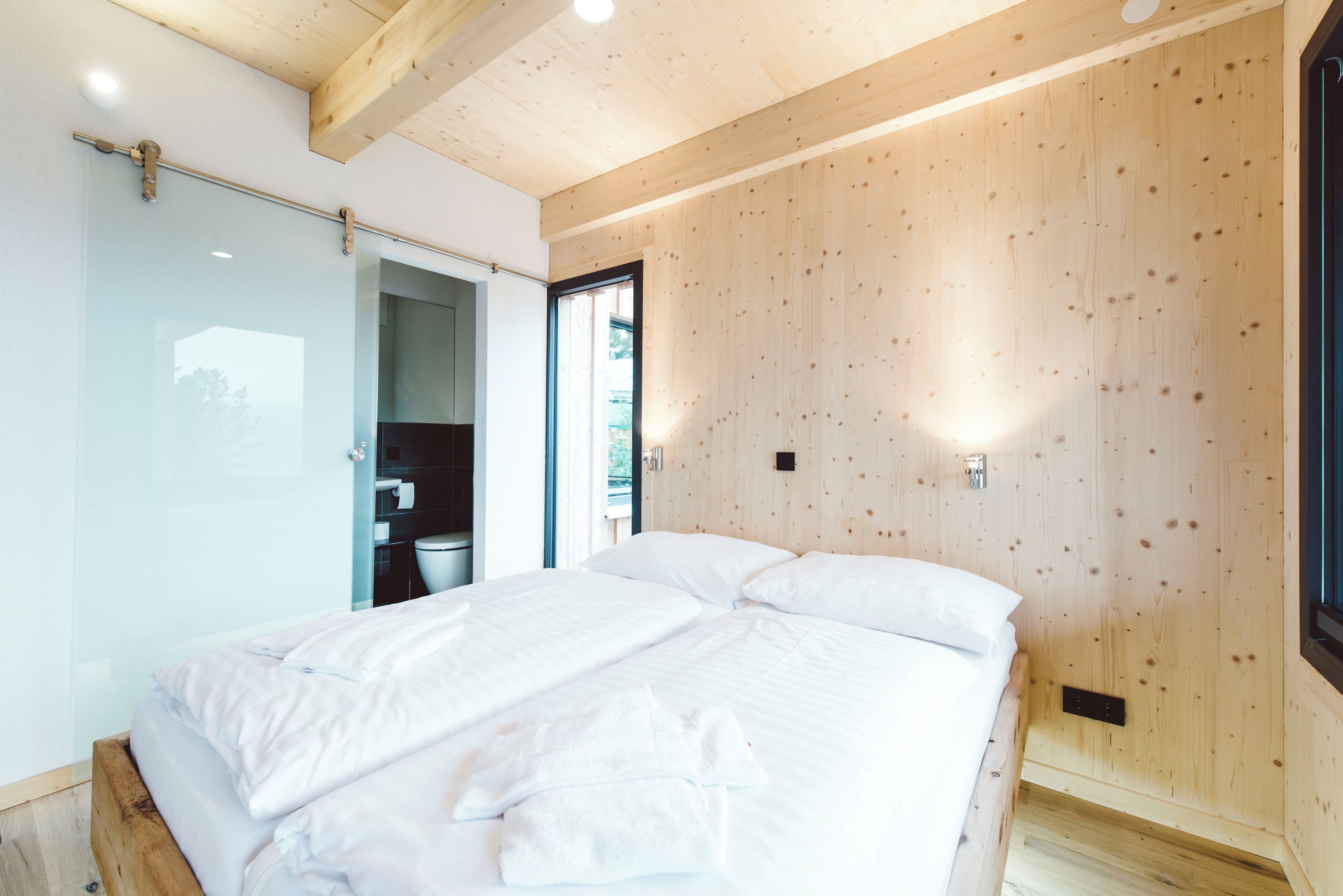 Un dormitorio con una cama grande, paredes de madera y un armario corredero que da a un baño.