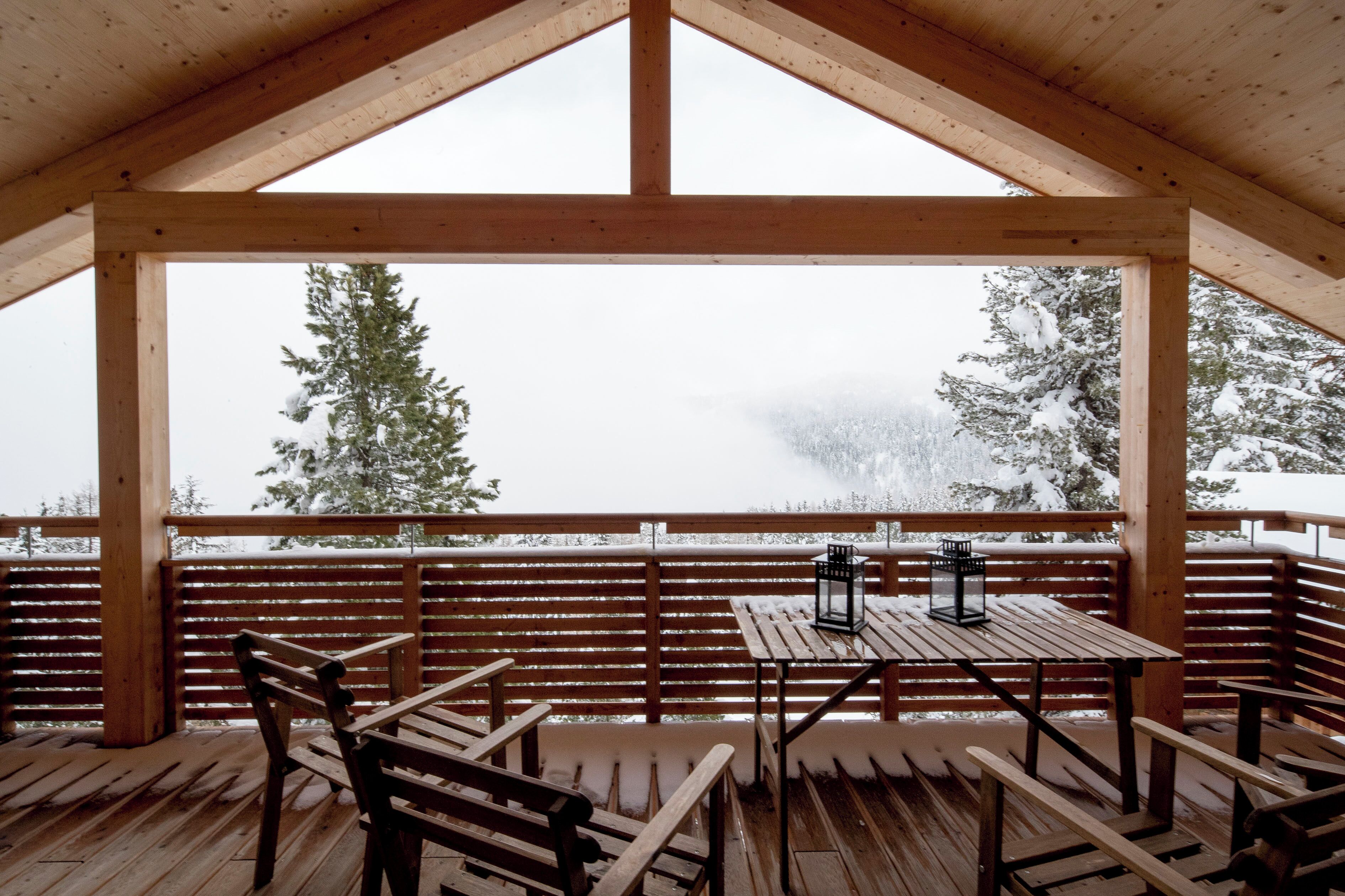 A wooden deck with a table and benches, overlooking a snowy landscape with trees.