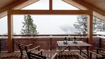 A wooden deck with a table and benches, overlooking a snowy landscape with trees.