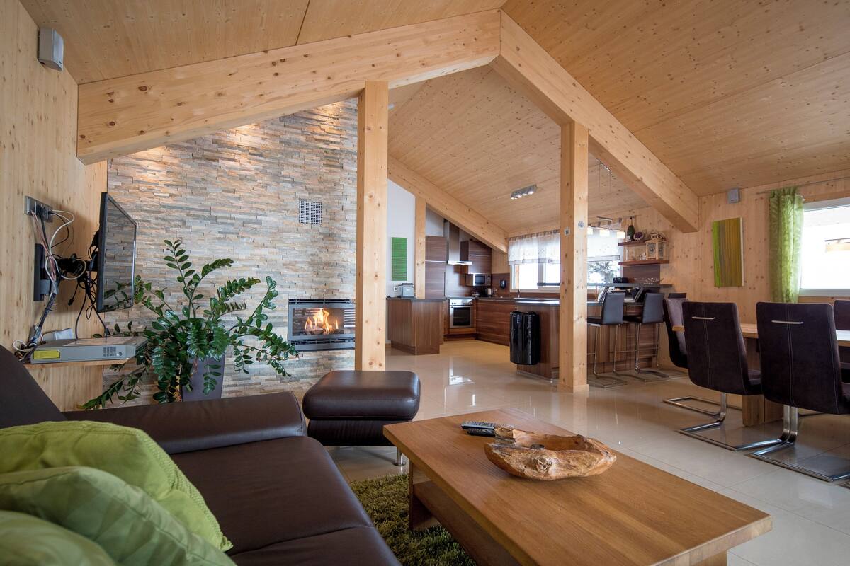 A modern living room with a fireplace, a sofa, a wooden coffee table, and a kitchen in the background.