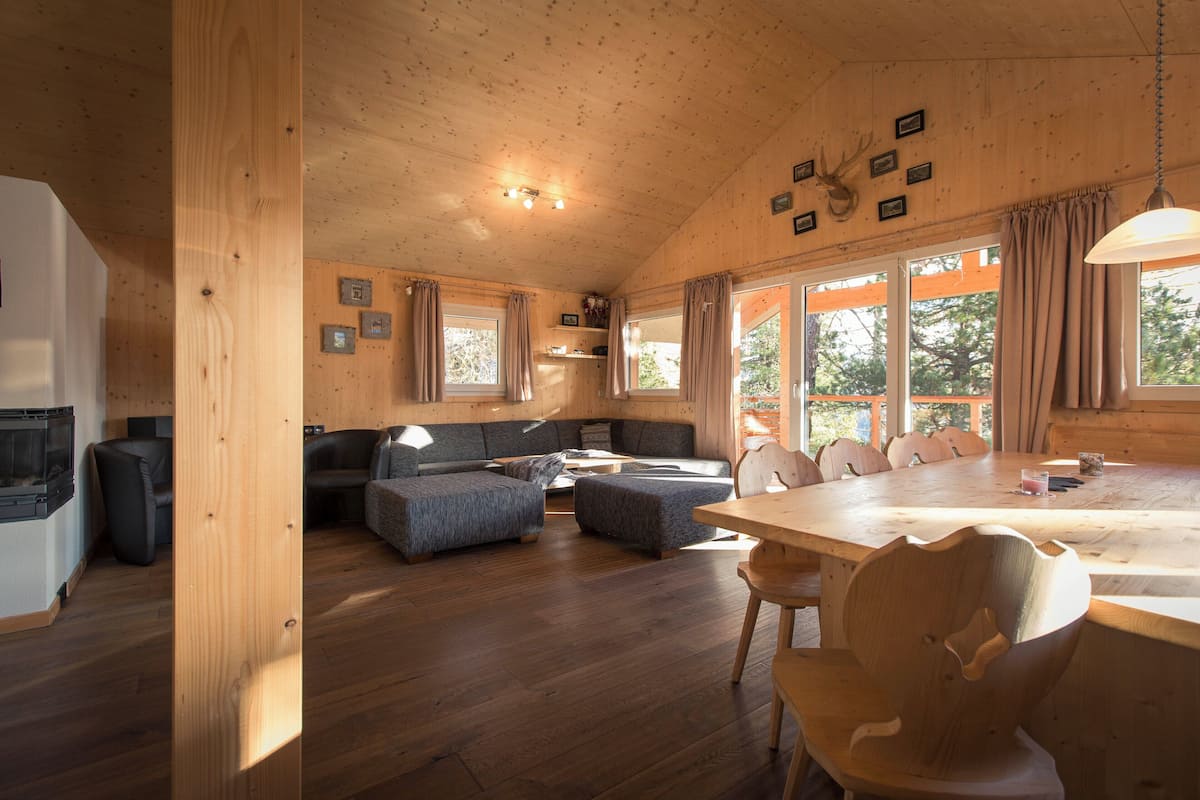 A cozy cabin interior with a wooden dining table, a sofa, and a fireplace.