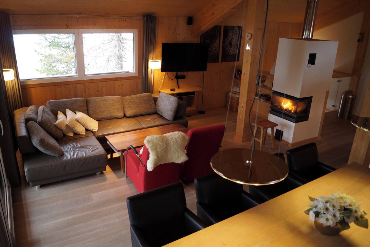 A cozy living room with a sofa, red chairs, a dining table, and a fireplace.