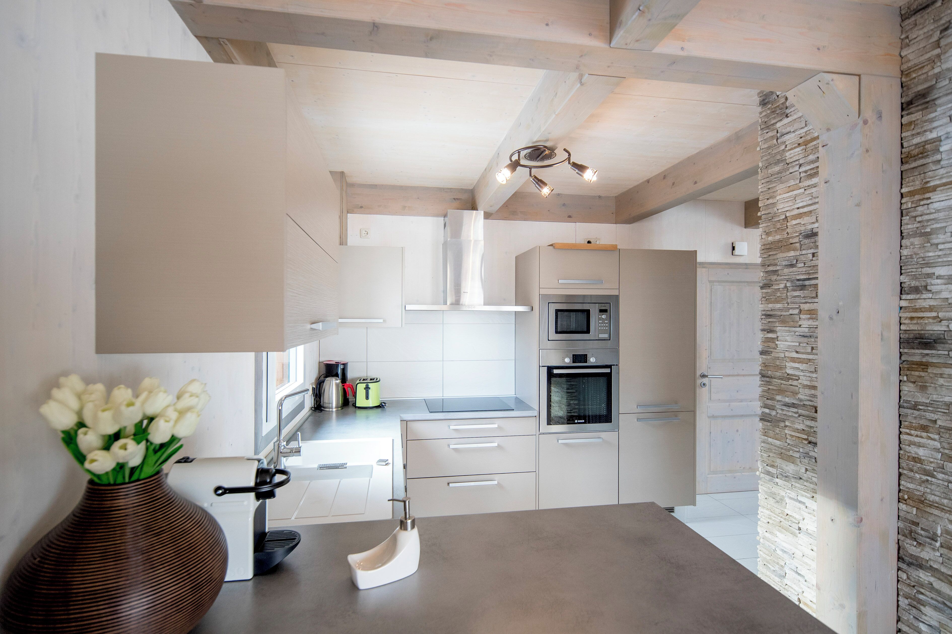 A modern kitchen with white cabinetry, a stone accent wall, and a wooden ceiling.