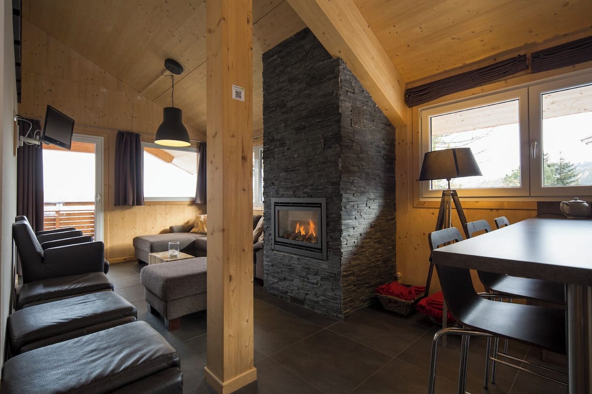 A cozy room with a stone fireplace, wooden beams, a sofa, and a dining area with chairs.