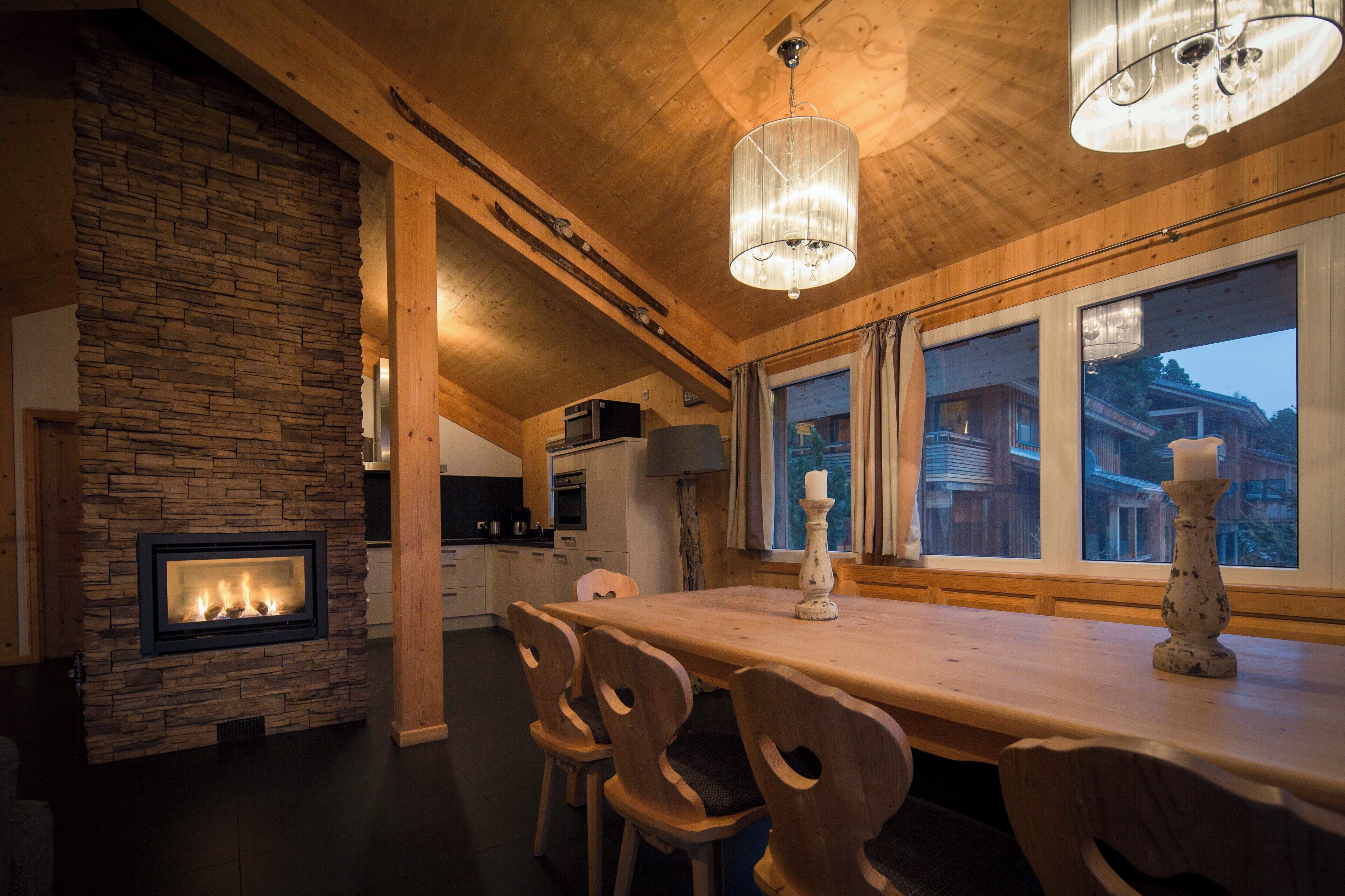 A cozy wooden interior with a stone fireplace, wooden dining table, and chairs.