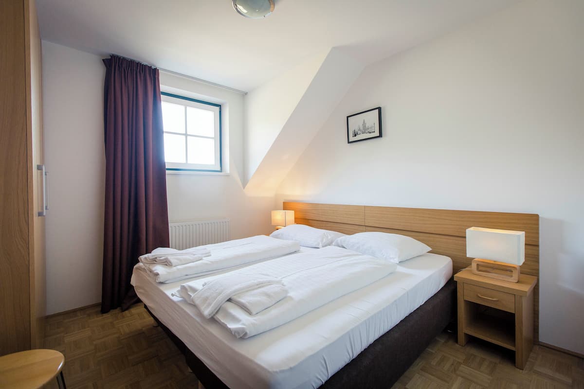 A hotel room with a large bed, a bedside table with a lamp, a window with curtains, and a picture on the wall.