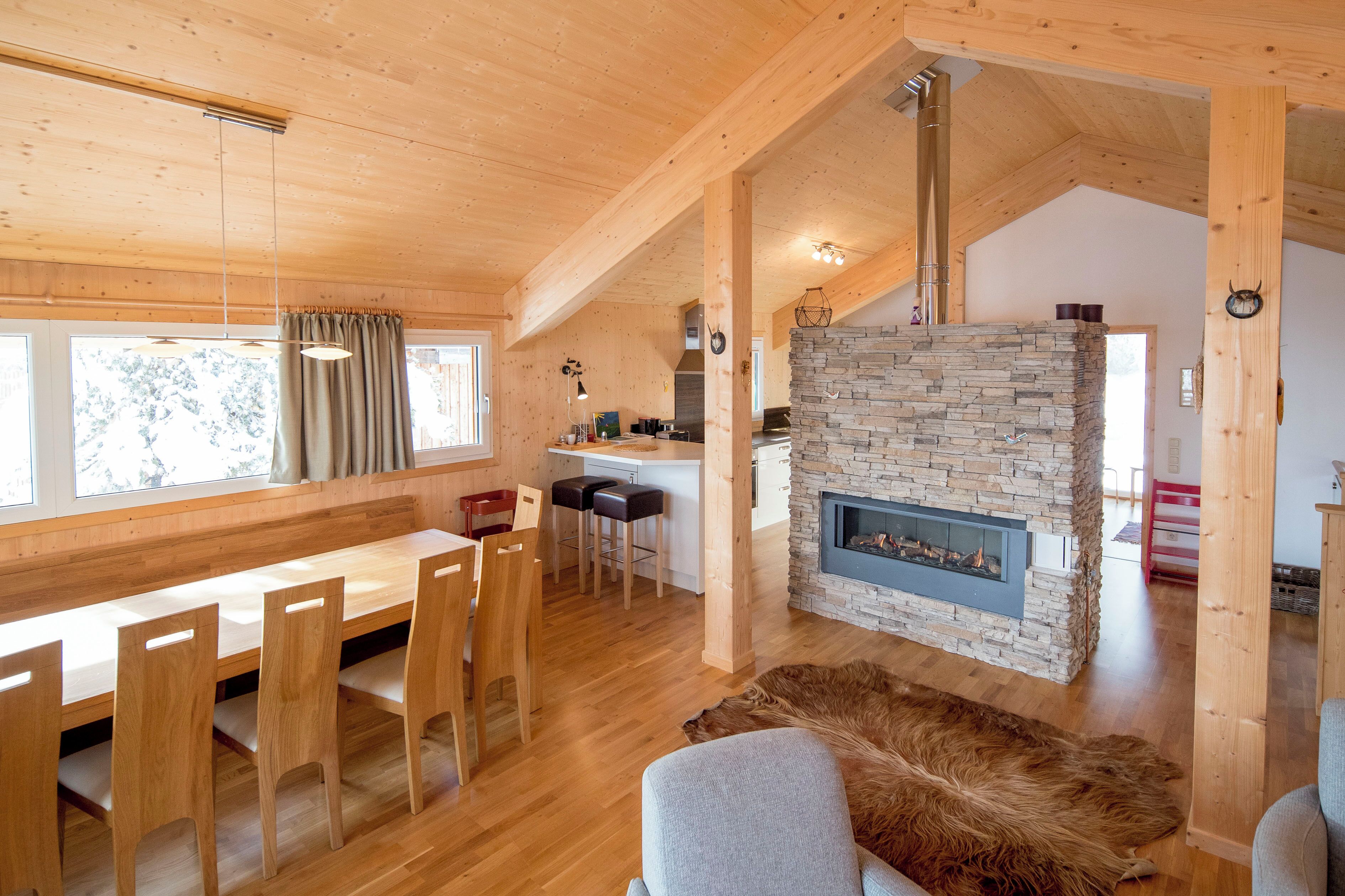 Un intérieur en bois avec une cheminée en pierre, un coin repas avec des chaises et un tapis en fourrure.