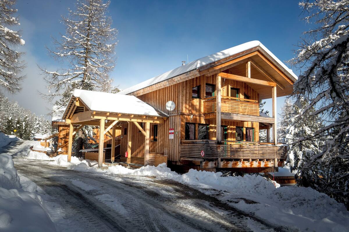 A wooden cabin with a balcony, surrounded by snow-covered trees.
