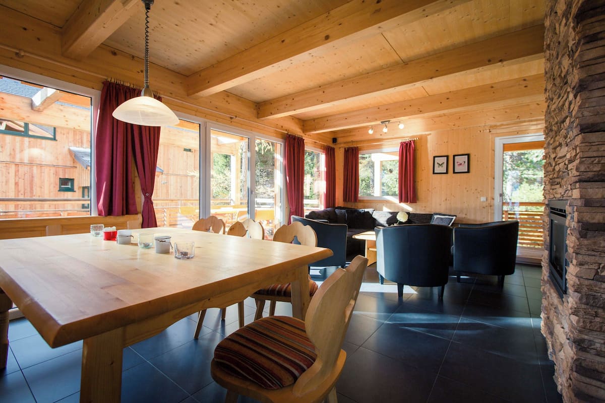A wooden interior with a dining table, chairs, sofas, and a stone fireplace.