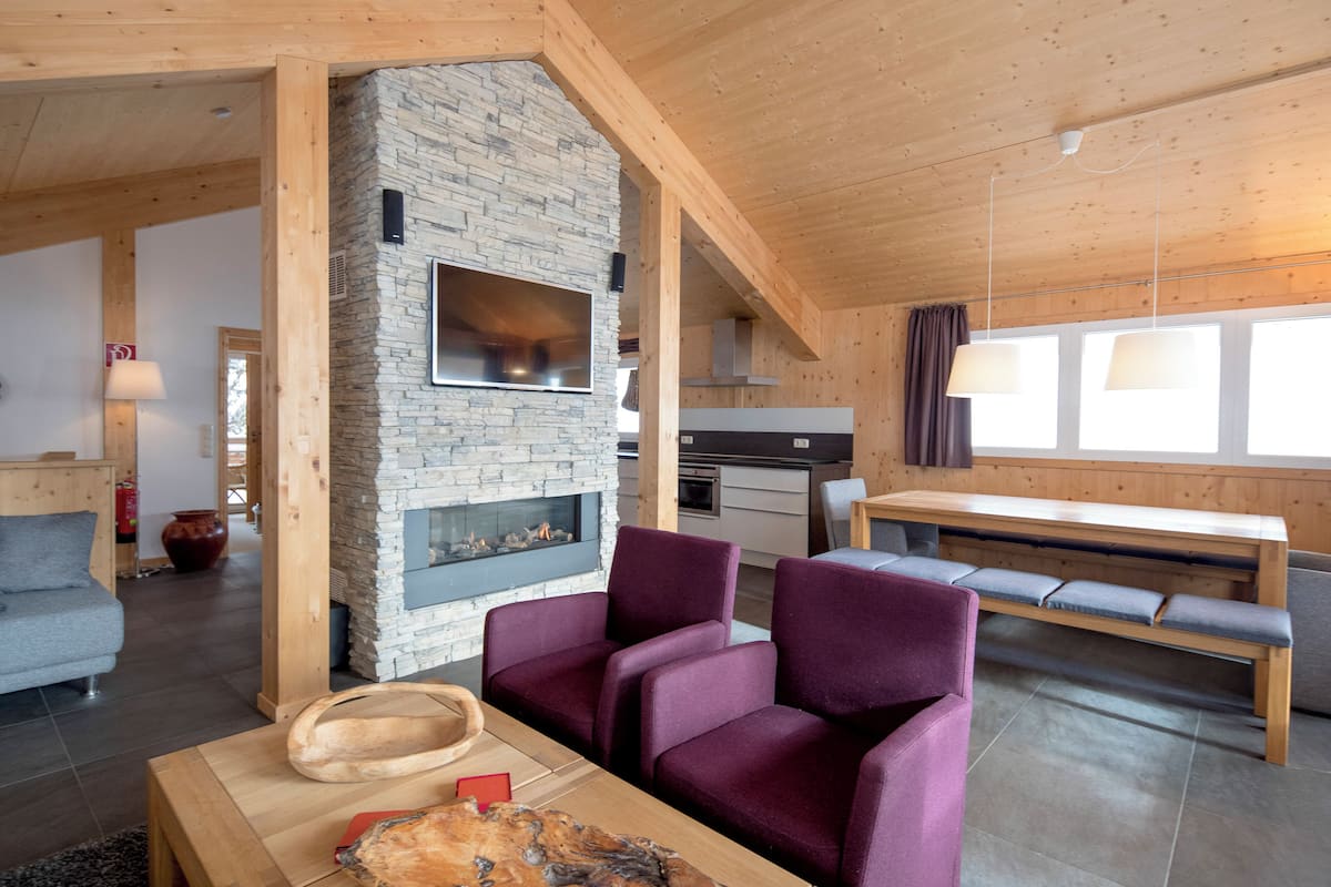 A modern living room with a stone fireplace, purple seating, and a wooden table.