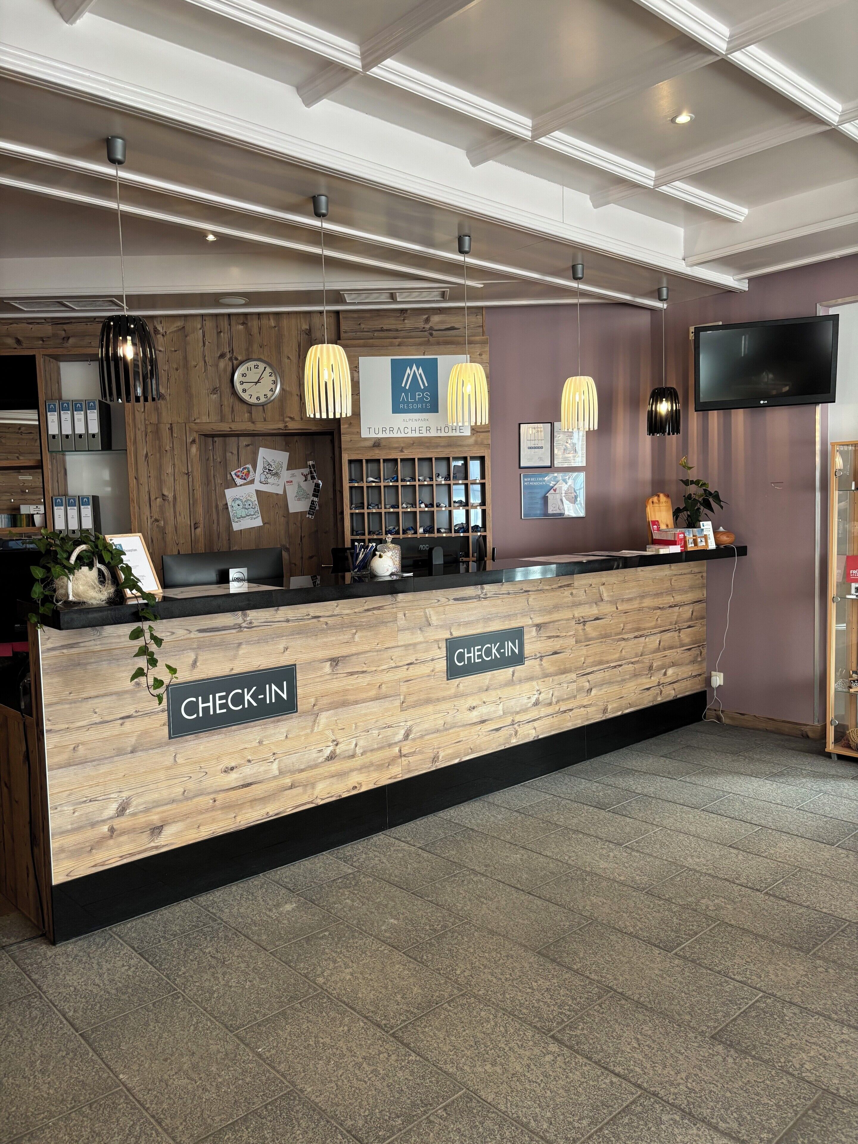 Ein Check-in-Schalter mit Holzausstattung, einer Wanduhr und einem Schild, das den Check-in-Bereich kennzeichnet.