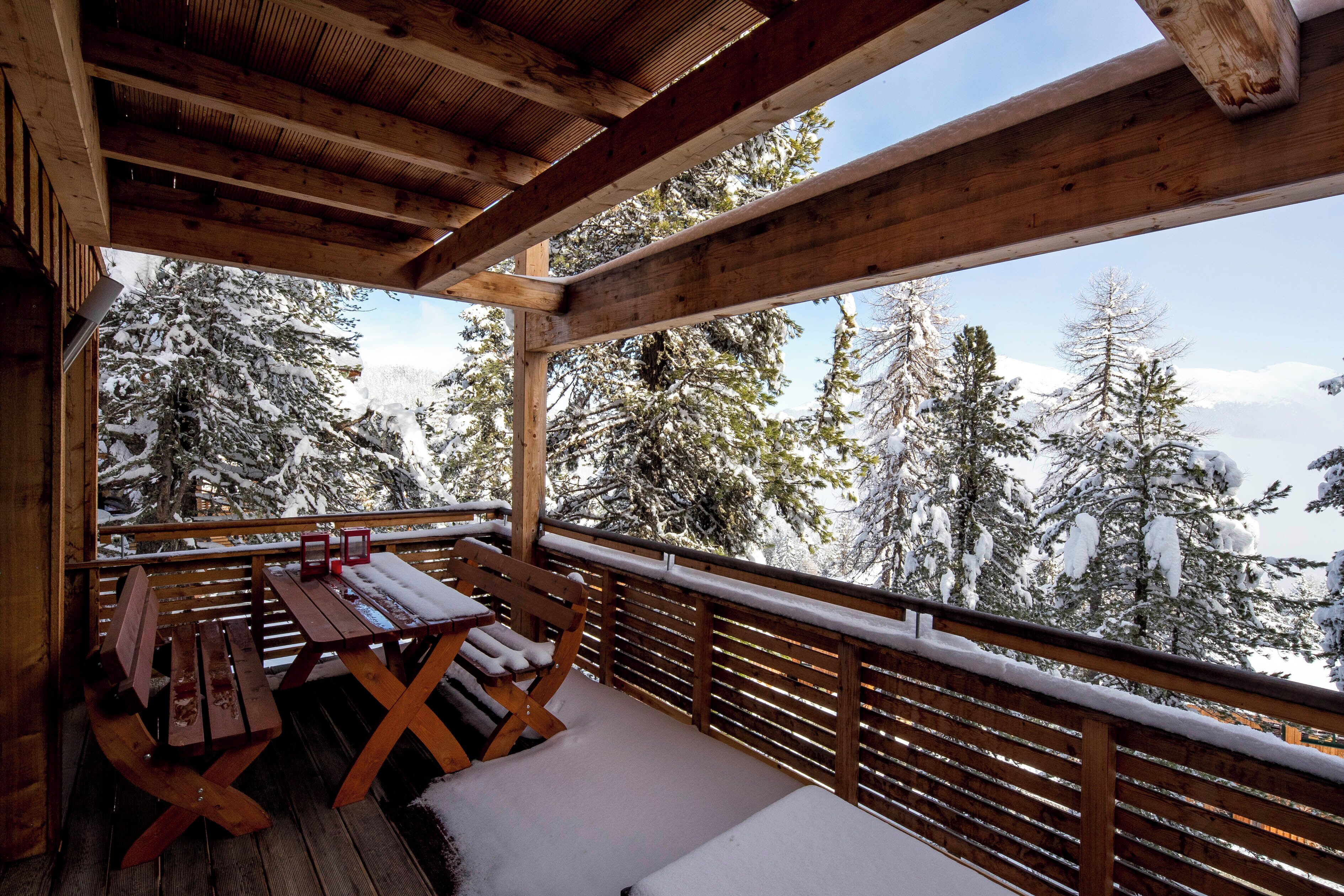 Une terrasse en bois avec une table et des bancs, d’où l’on peut admirer les arbres couverts de neige.