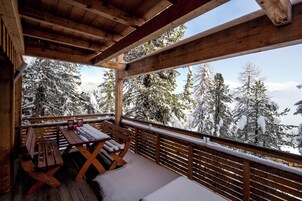 Una terraza de madera con una mesa y bancos, con vistas a árboles cubiertos de nieve.