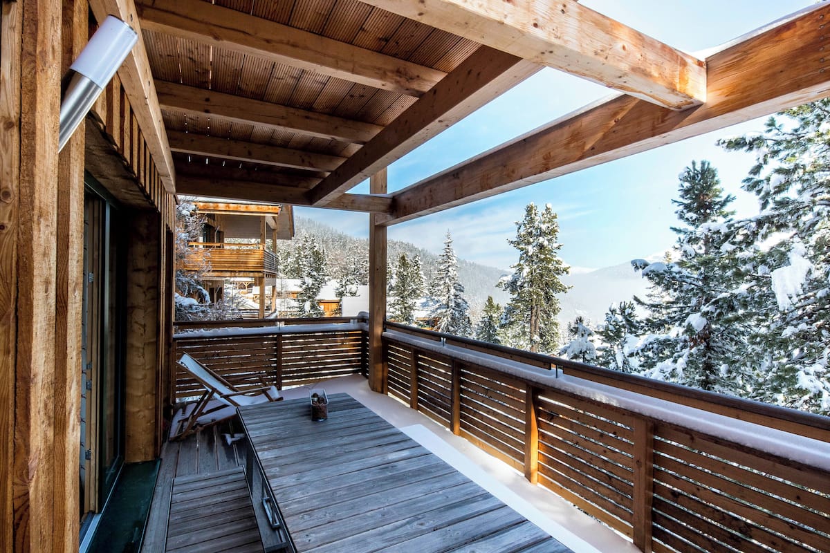 A wooden deck with a view of snow-covered trees and mountains.