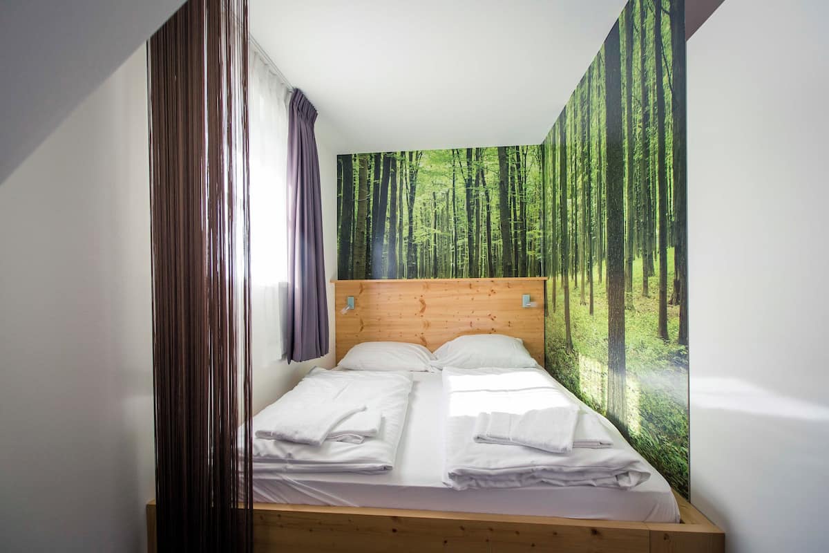 A bedroom with a bed, wooden headboard, and a forest-themed wall mural.